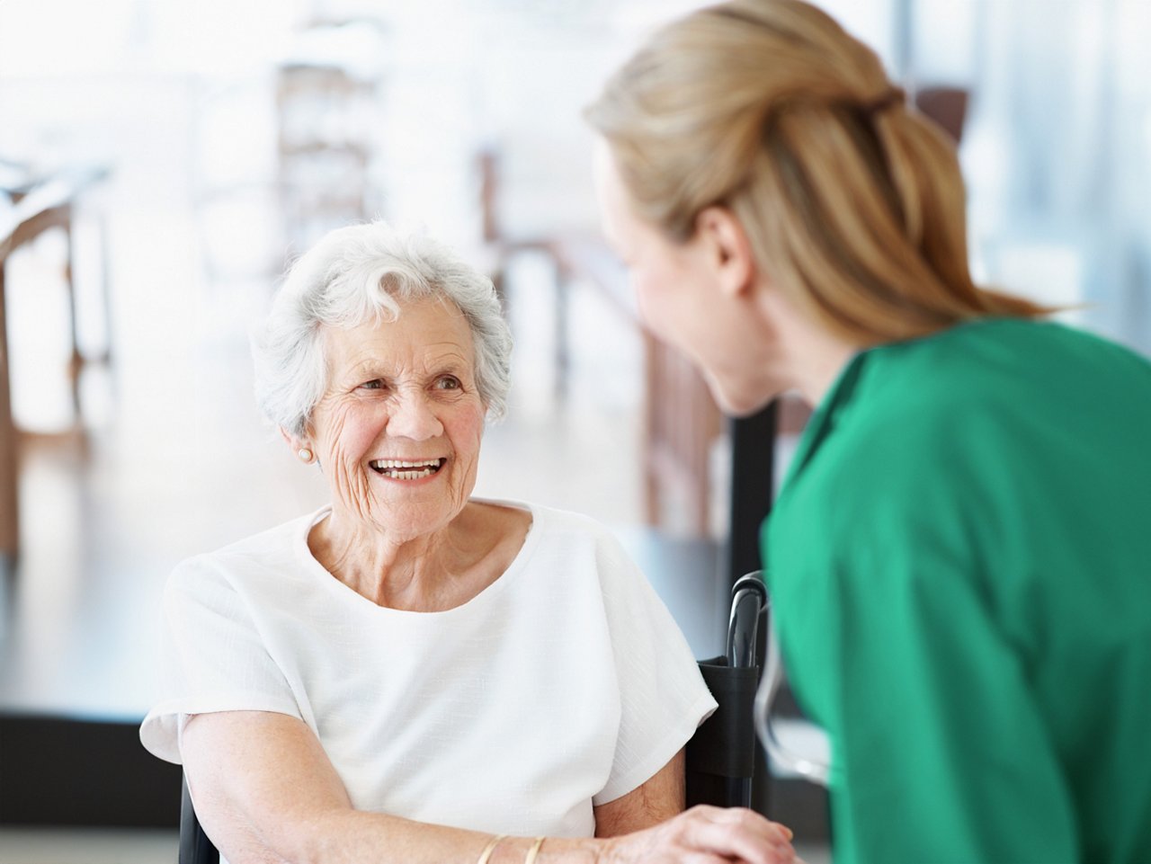 An elderly woman in a wheel chair smiling at a female clinician in a green shirt.