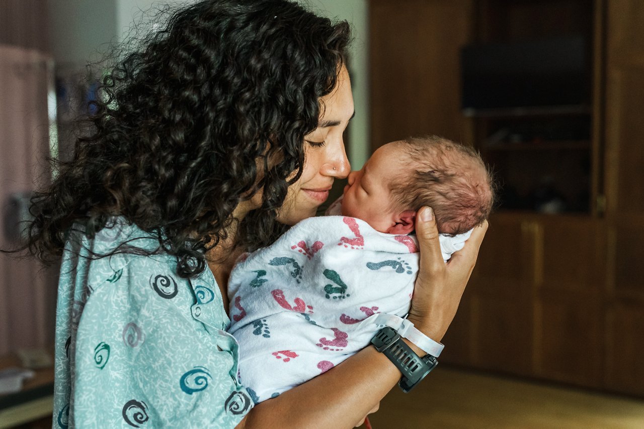 New mom nuzzeling her newborn baby in a hospital room.