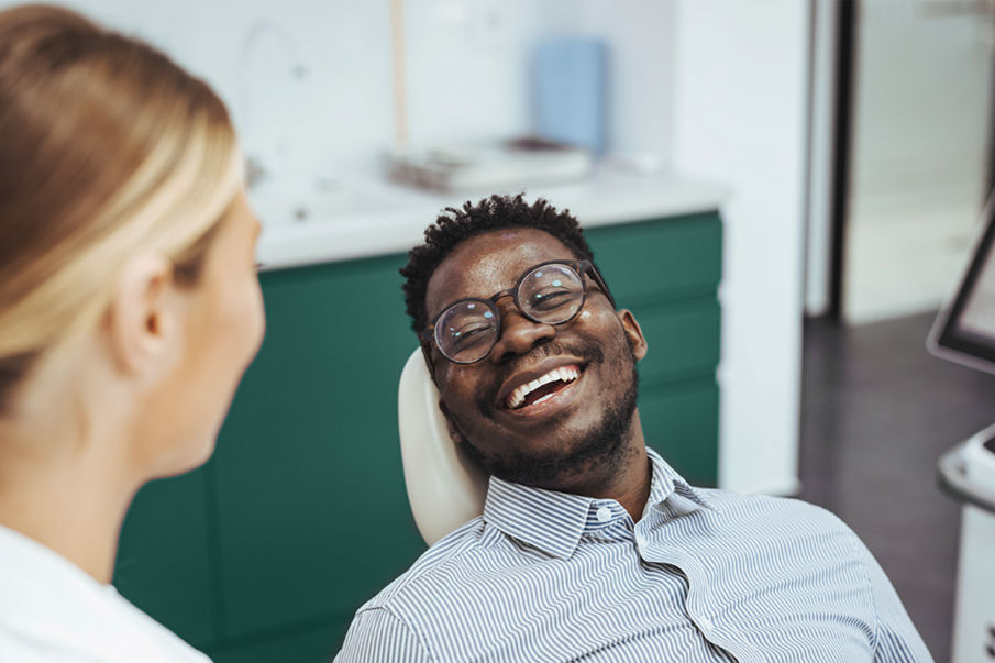 Smiling african guy in dentist chair looking with trust at his doctor, close up. Young African American Man Getting Teeth Treatment With Professional Stomatologist At Modern Clinic