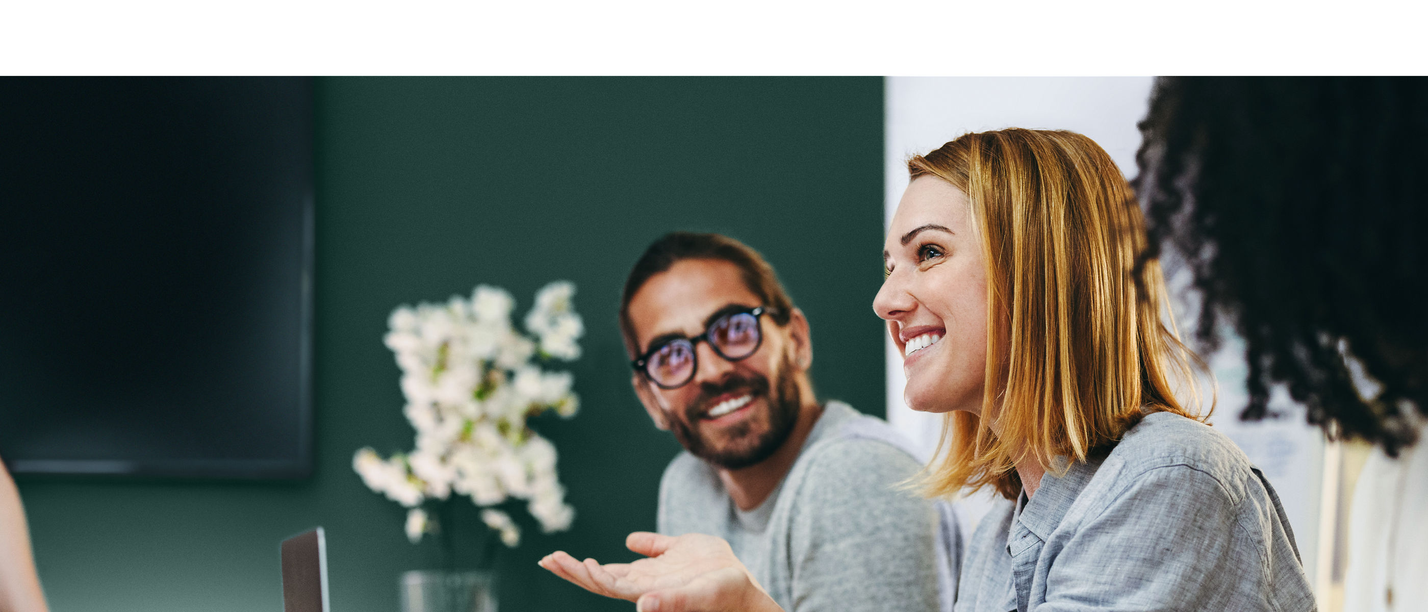 Several smiling colleagues conversing in a conference room. One of them is standing and the others are seated at a conference table.