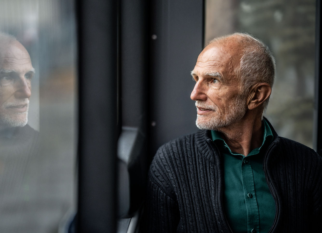 Older man looking out the window while seated on a bus.