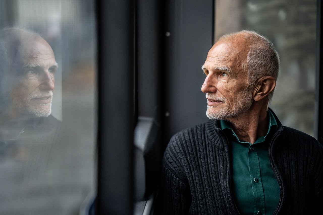 Older man looking out the window while seated on a bus.