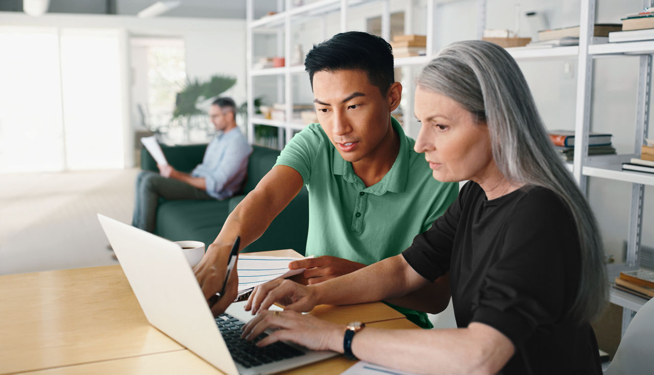 A female employee typing on her laptop and a male colleague interacting with her and pointing at the screen.
