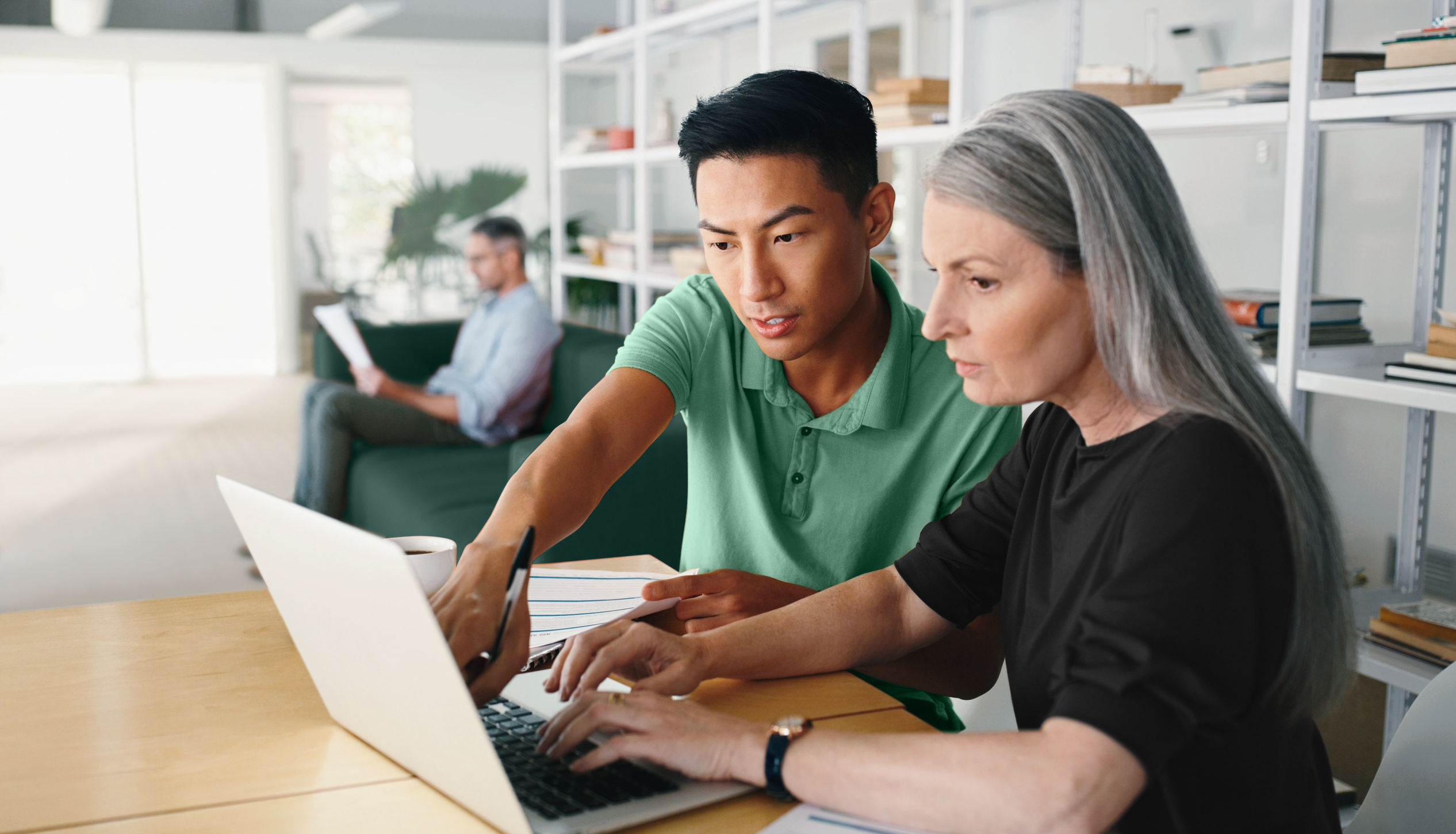 A female employee typing on her laptop and a male colleague interacting with her and pointing at the screen.