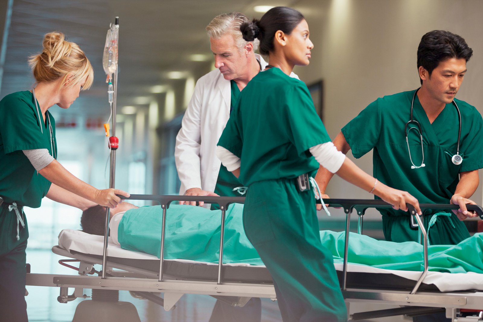 A team of four clinicians rushing a patient on a stretcher down a hospital hallway.