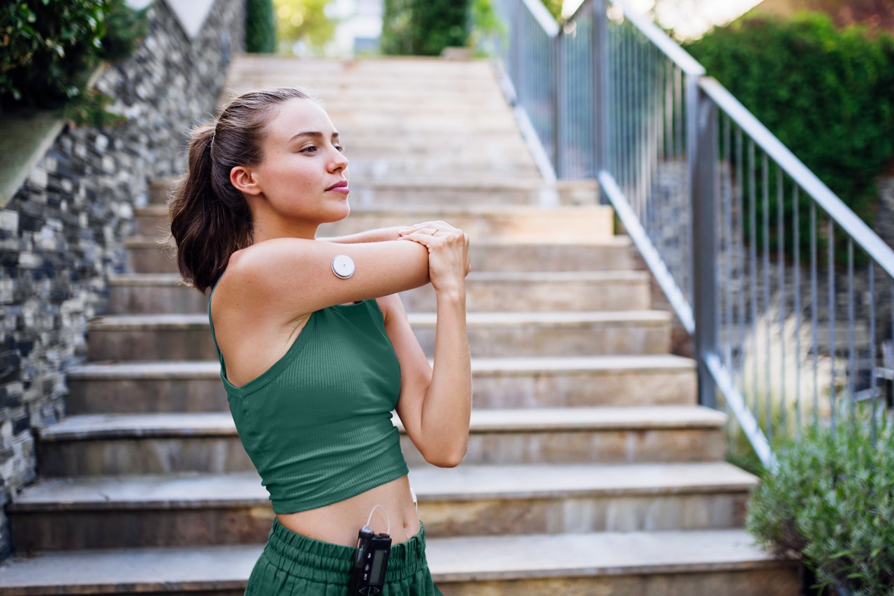 Beautiful diabetic woman preparing for outdoor run in the city. Young woman wearing an insulin pump during exercising. Concept of exercise and diabetes.