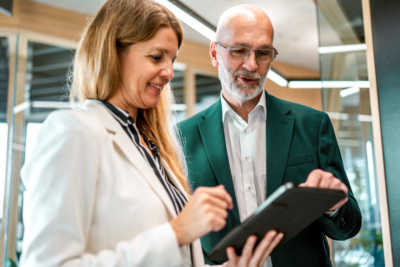 Two employees having a conversation while viewing a tablet in a meeting room.