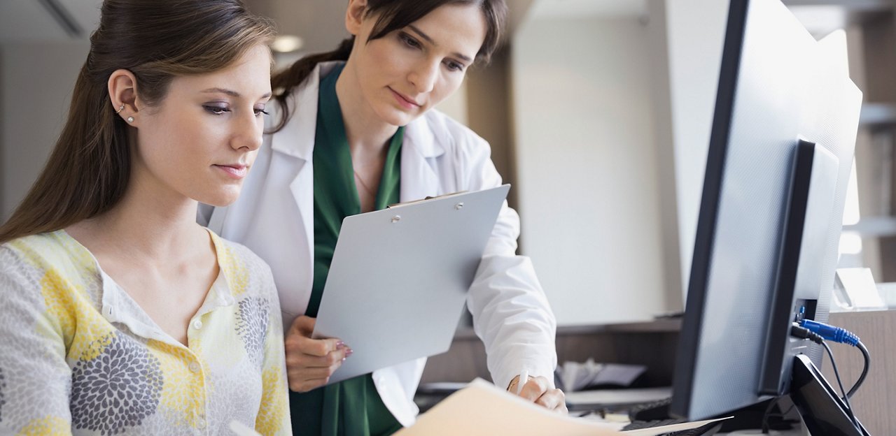 A clinician with a clipboard looking over files with an administrator.