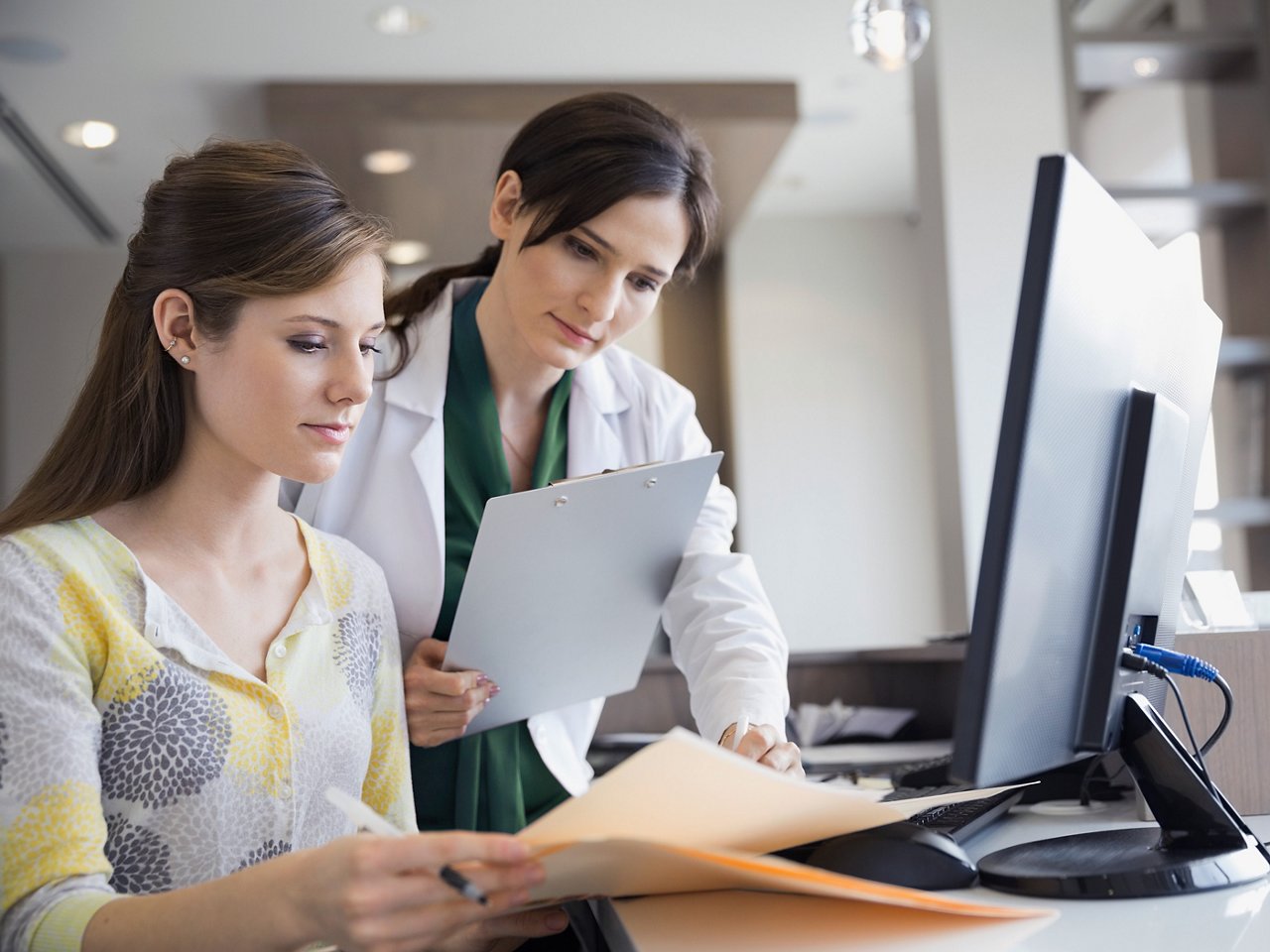 A clinician with a clipboard looking over files with an administrator.