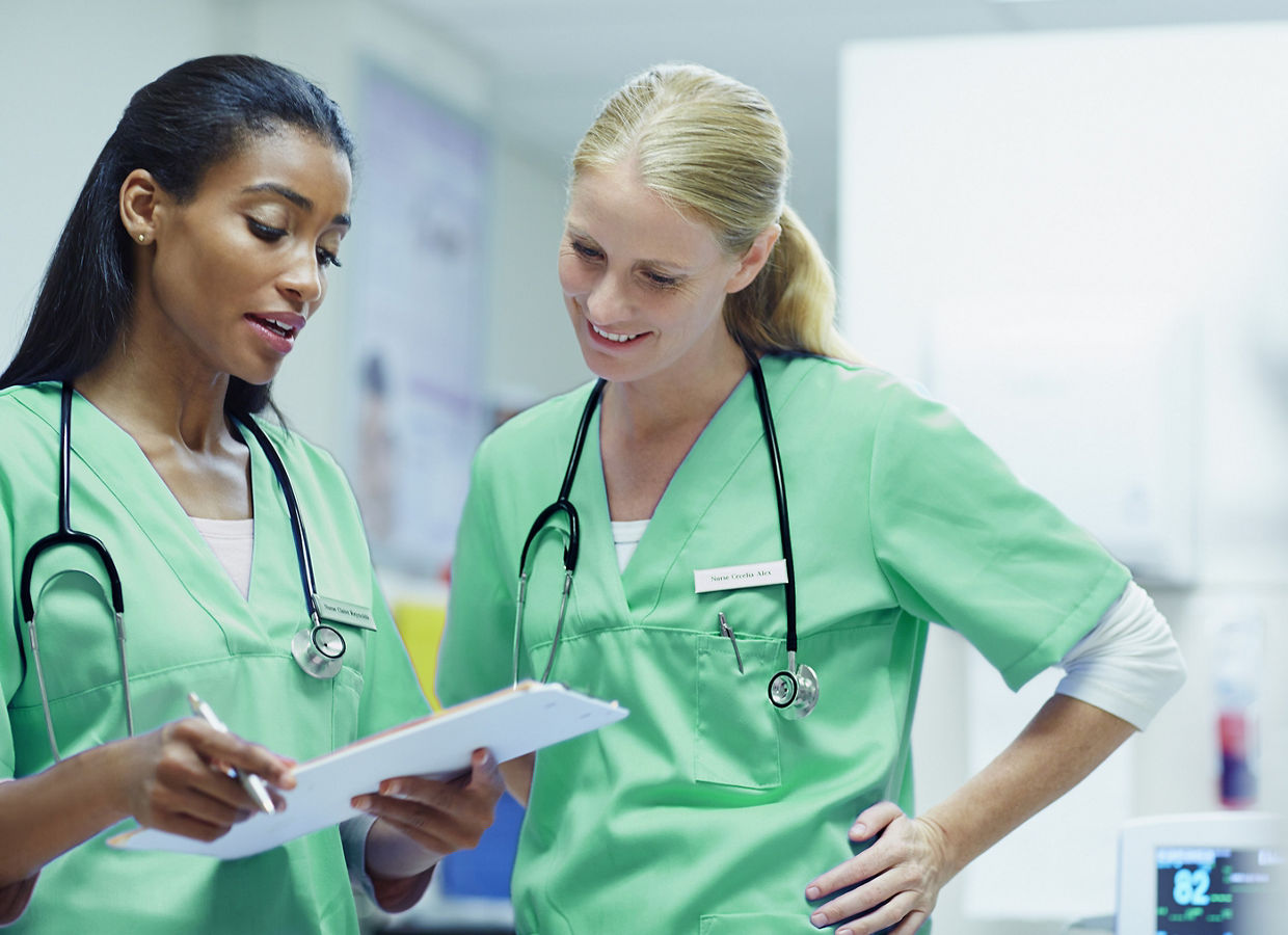 Two female clinicians looking at a file on a clipboard.