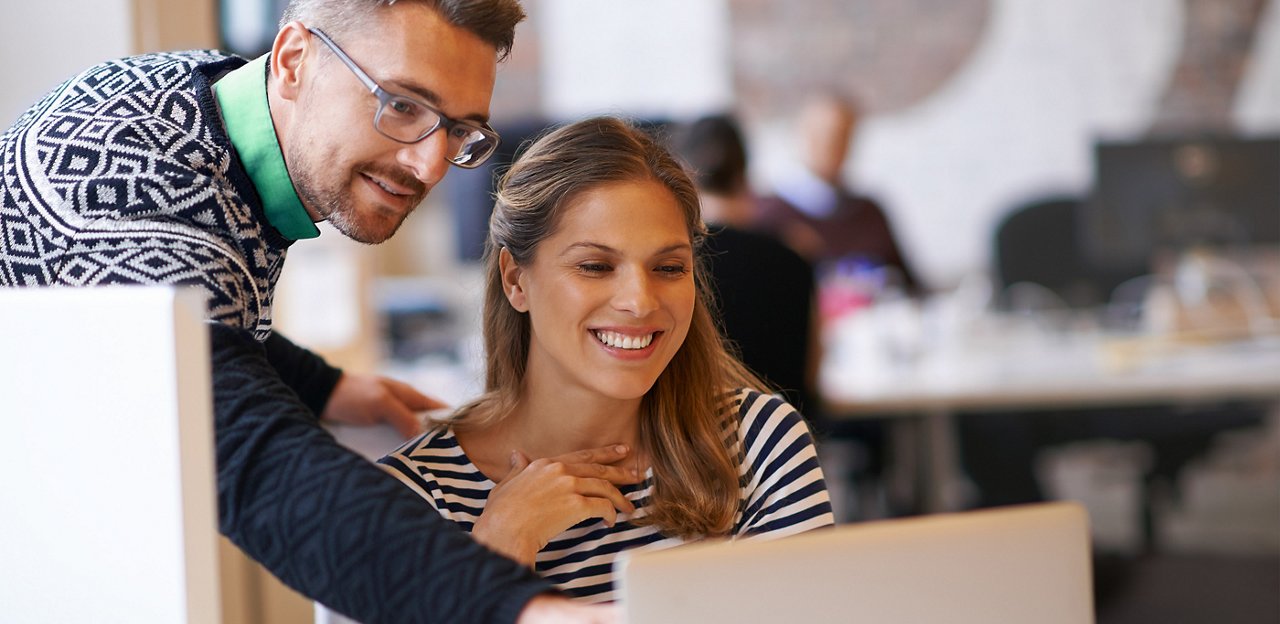 A man and woman looking at a laptop and smiling while the man points to something on the screen.