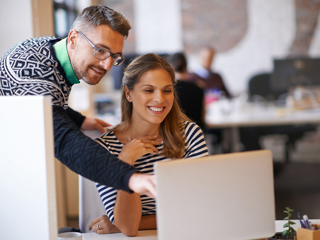 A man and woman looking at a laptop and smiling while the man points to something on the screen.