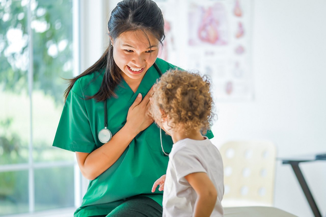 A smiling female clinician with her hand over her heart talking with a toddler