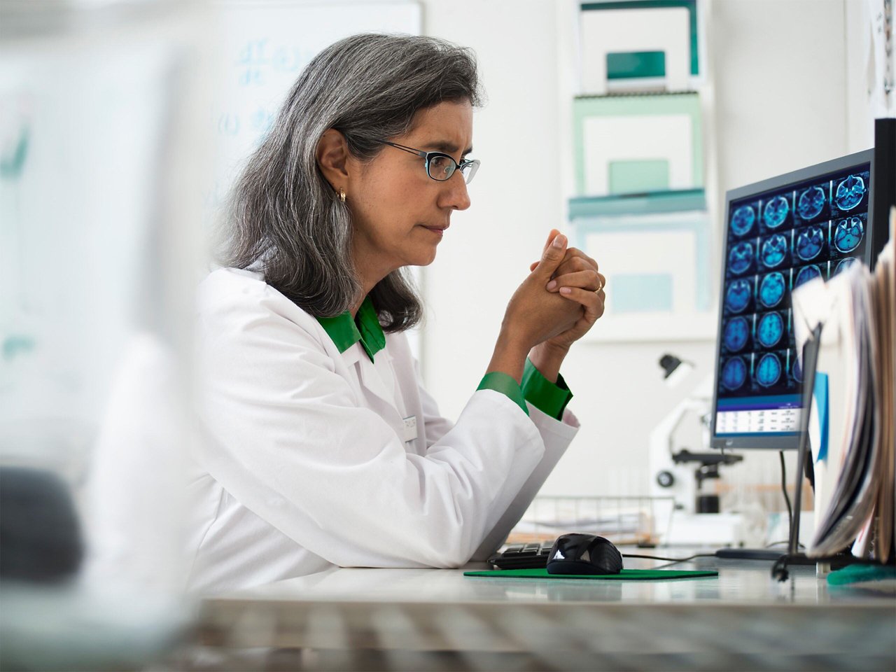 Un medico seduto alla scrivania nel suo ufficio, che guarda un monitor del computer con più immagini craniche