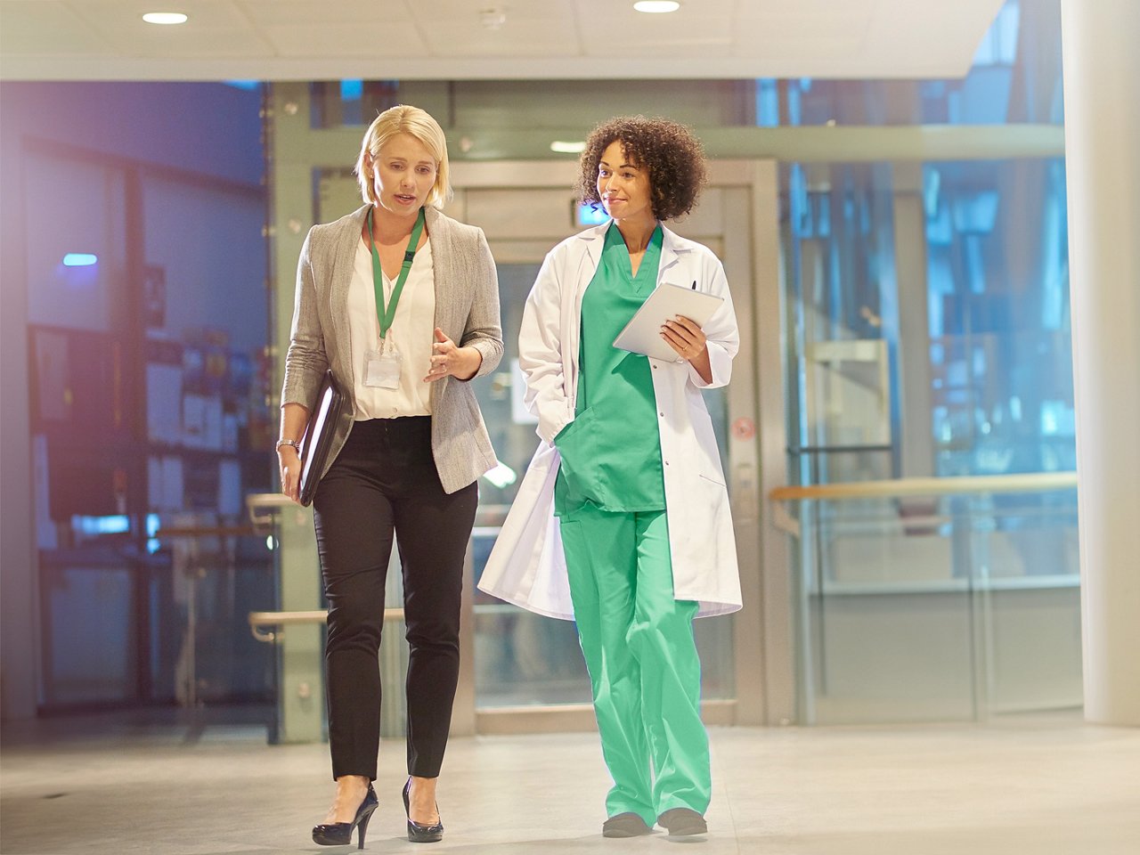 A female business leader talking with a female clinician as they walk down a hallway