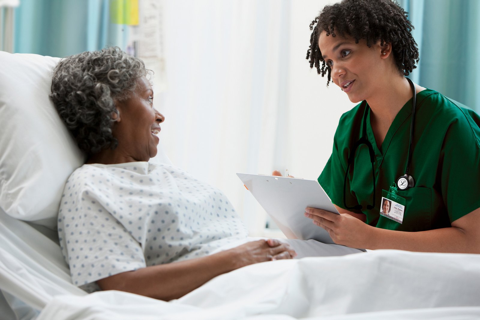 A female clinician smiling while asking an older female patient questions and writing down her answers