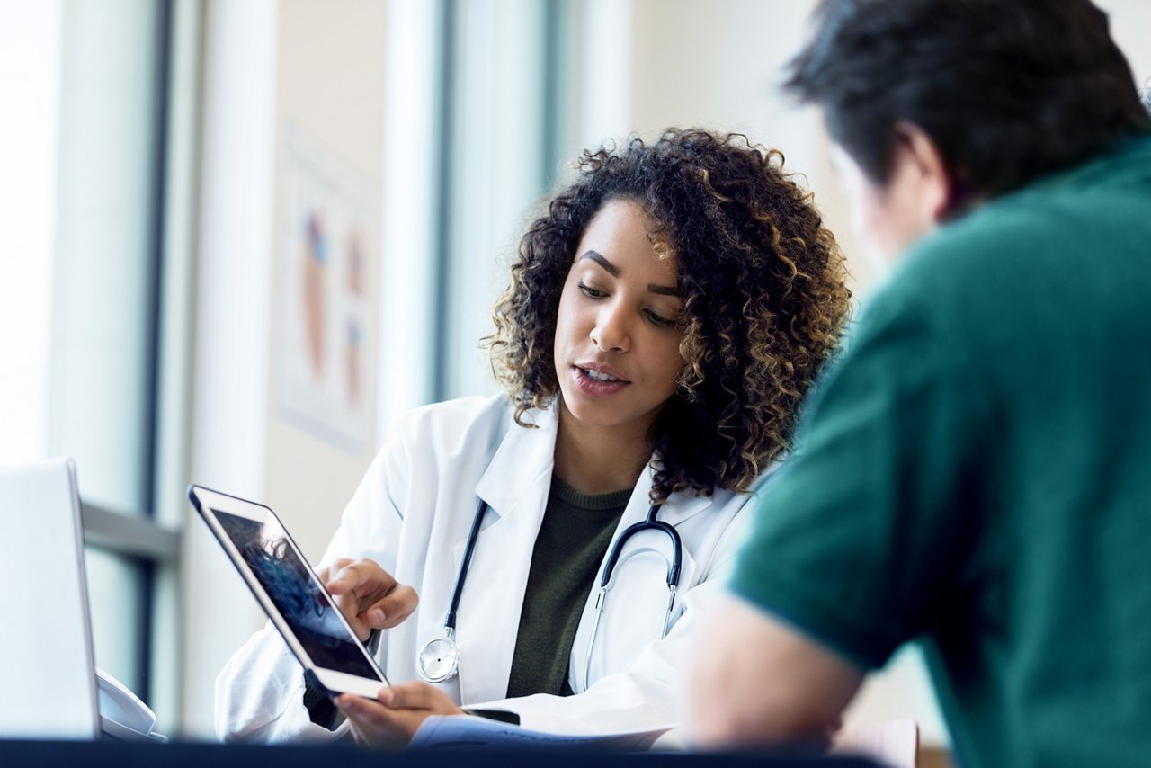 Doctor and nurse collaborating while viewing content on a tablet in a conference room.