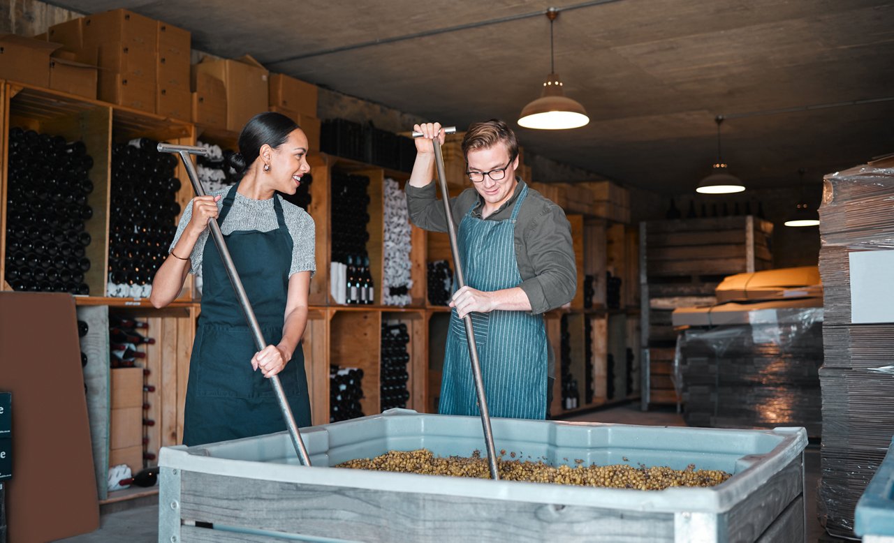 Man and woman winery workers making wine with a fruit press tool or equipment in warehouse or distillery.