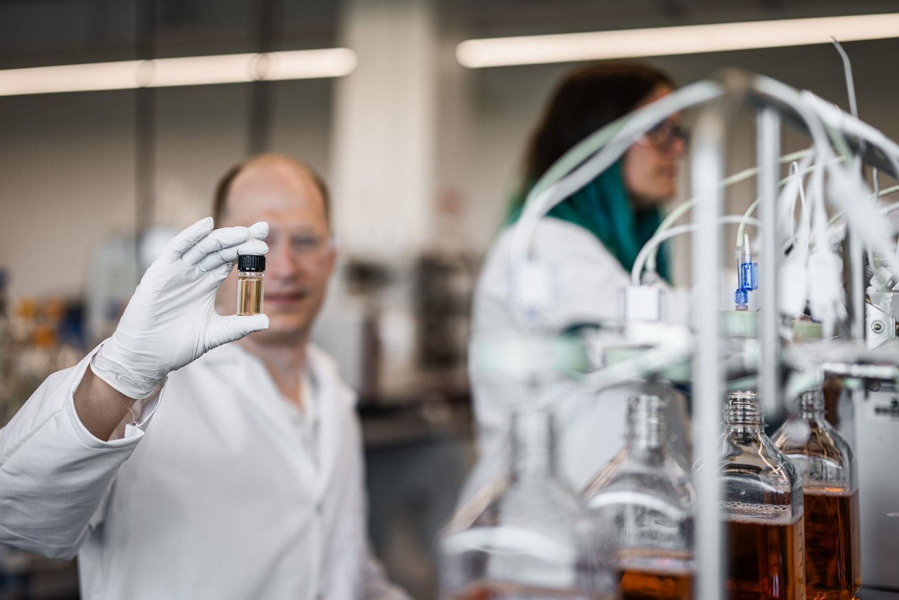 Image of two lab workers, one examining vial of liquid.