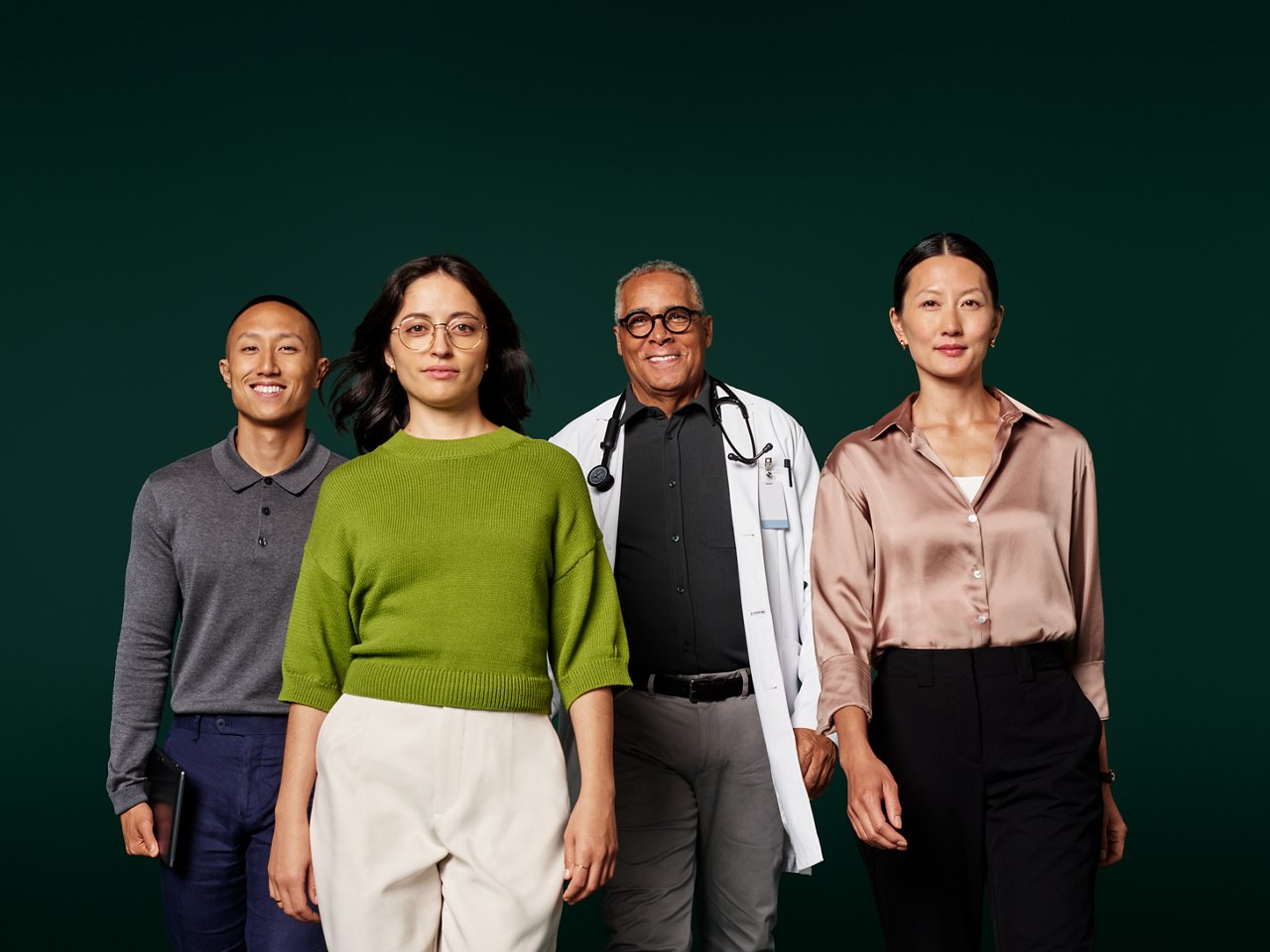 Group portrait of four health information systems professionals walking in a group toward camera on a dark green background.