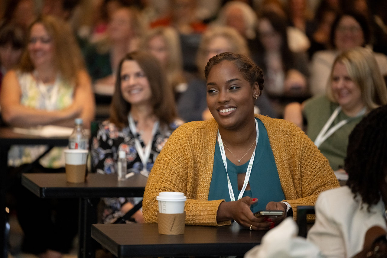 Attendee seated in crowd smiling at 2025 Client Experience Summit (CES)