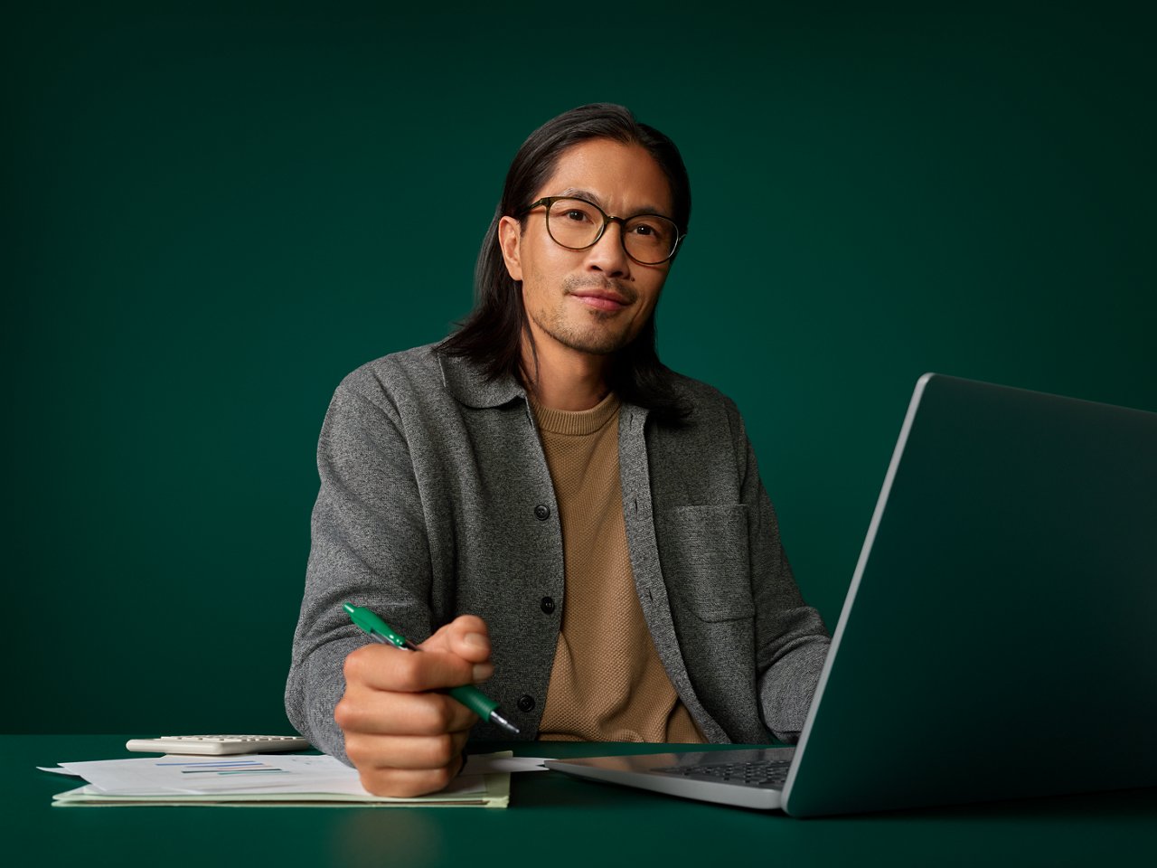 Portrait of a male hospital buyer at his desk on a dark green background.