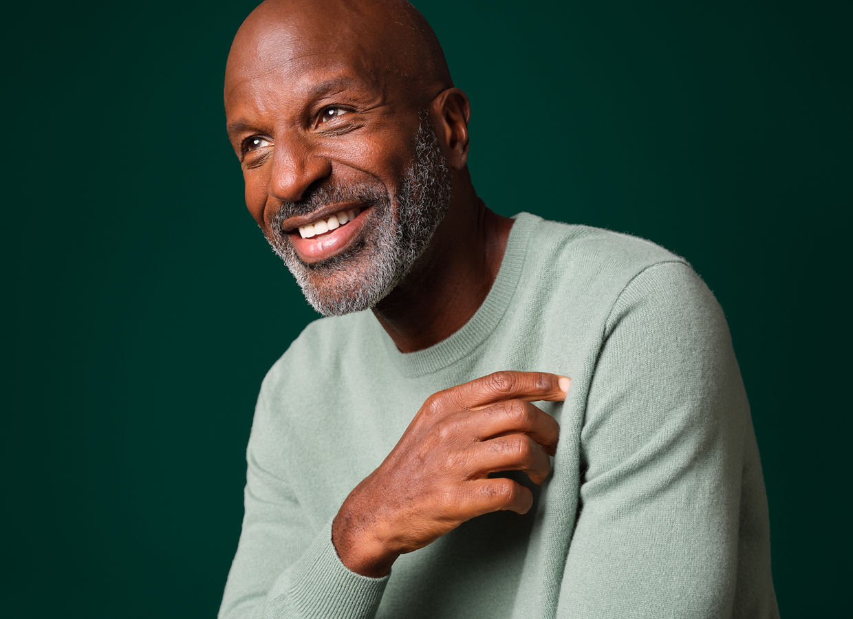 A smiling man who is seated with his hand near his chin.