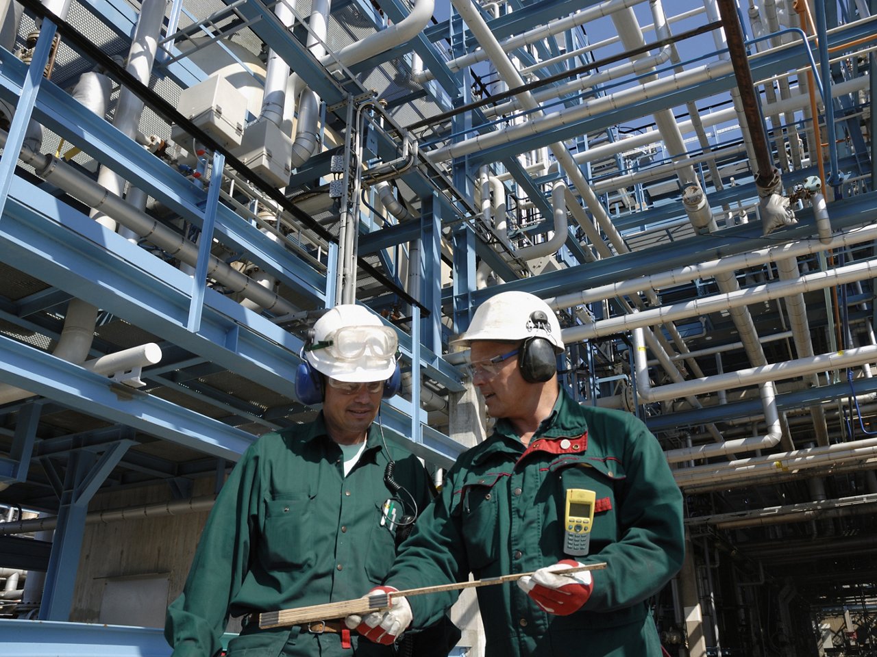 two engineers with hard-hats standing in front of refinery and miles of pipelines