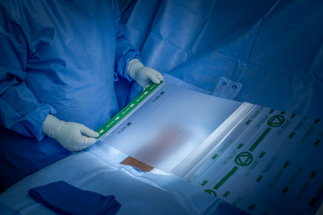 A OR nurse holds the Ioban™ CHG Incise Drape by its handles over a patient's abdomen.
