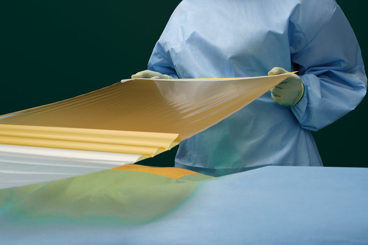 A nurse in an operating room pulls a sheet of 3M Ioban 2 Antimicrobial Incise Drape over the patient for surgery prep.