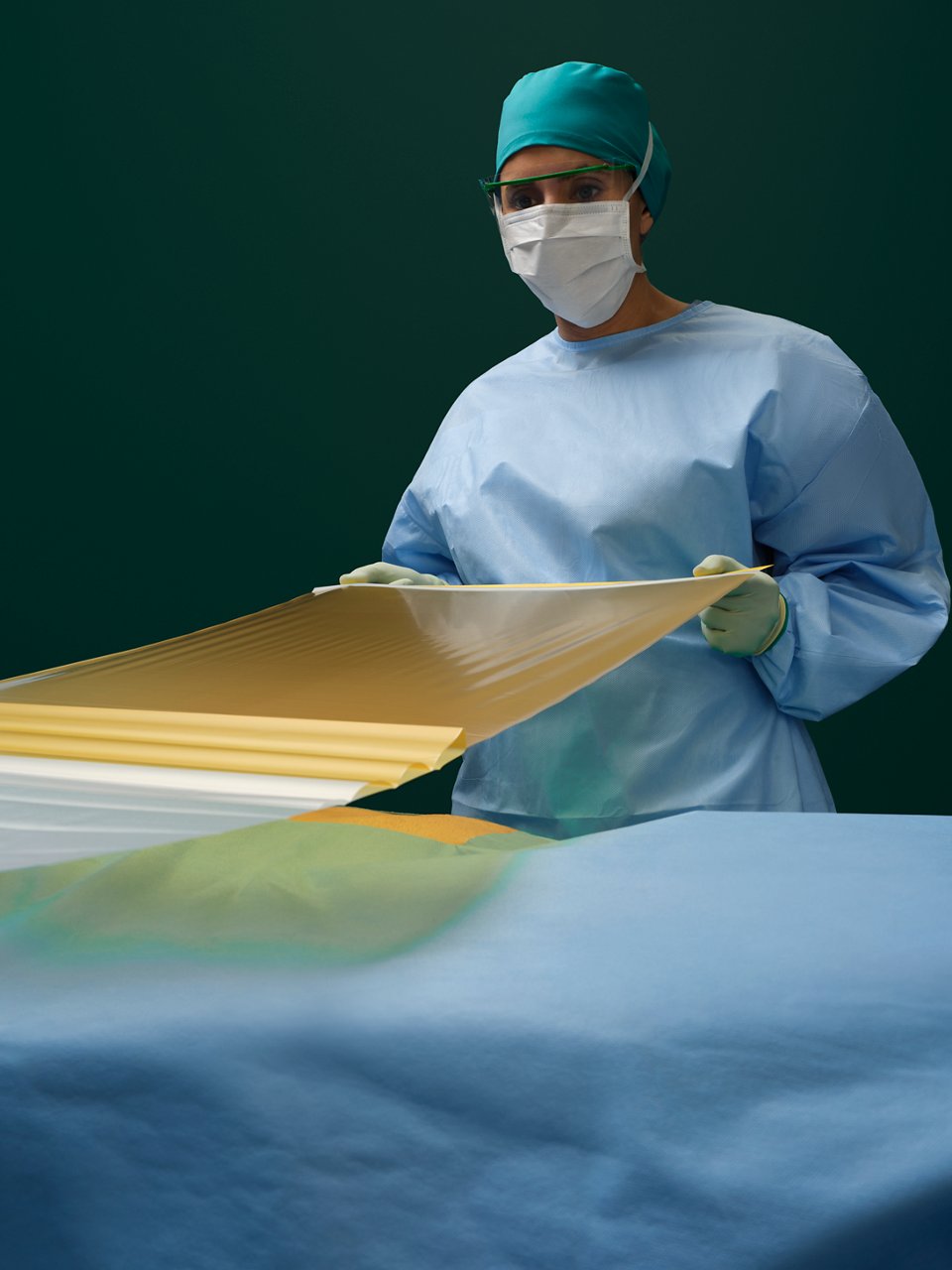 A nurse in an operating room pulls a sheet of 3M Ioban 2 Antimicrobial Incise Drape over the patient for surgery prep.
