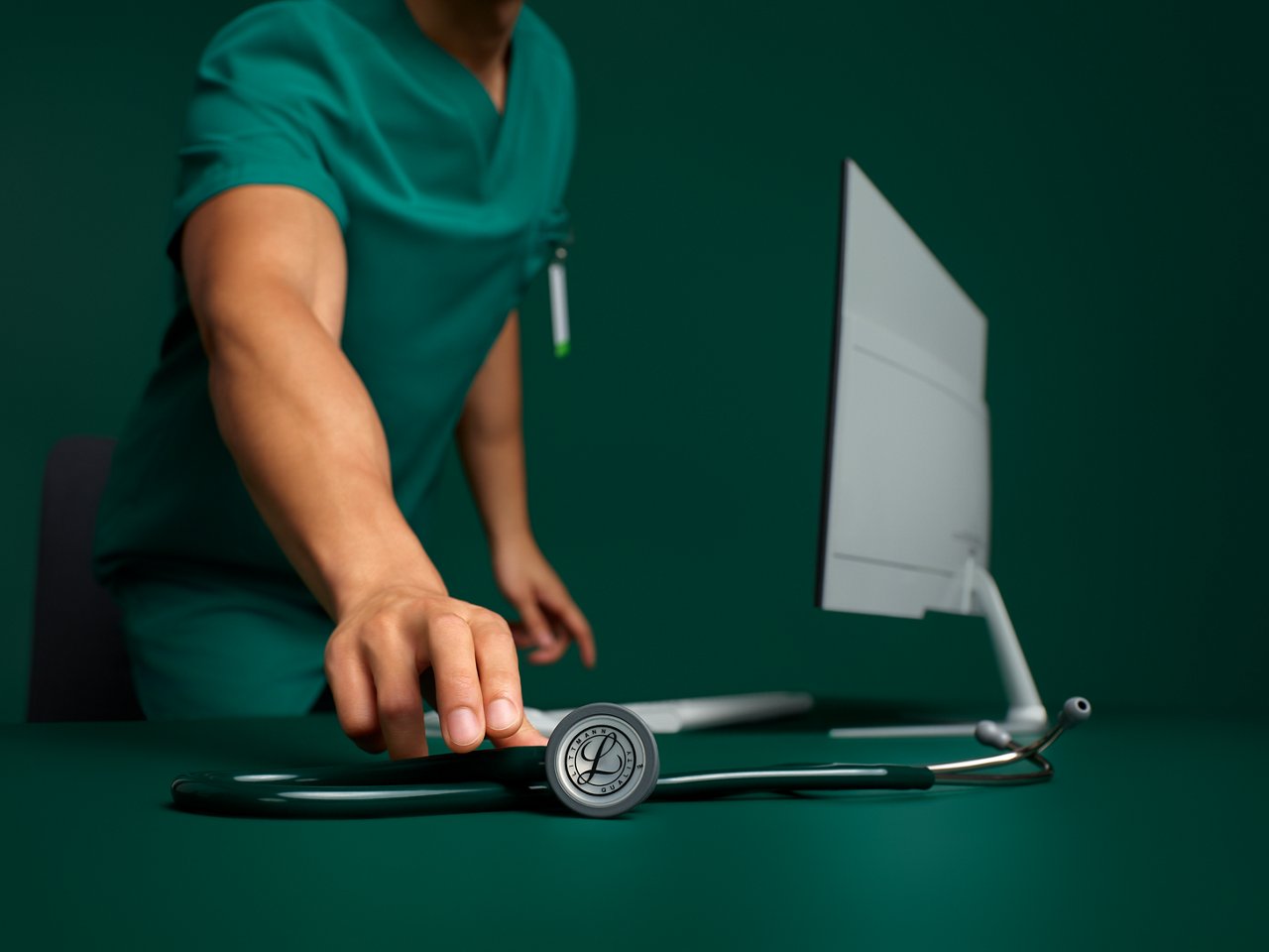 Ritratto di un infermiere in divisa che prende uno stetoscopio Littmann da una scrivania su uno sfondo verde scuro.