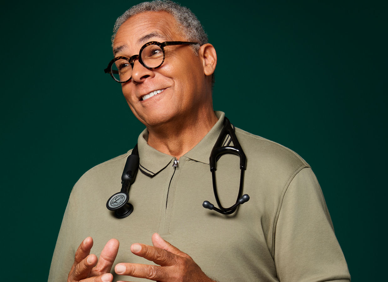Portrait of a male primary care doctor with Littmann stethoscope around his neck on a dark green background.