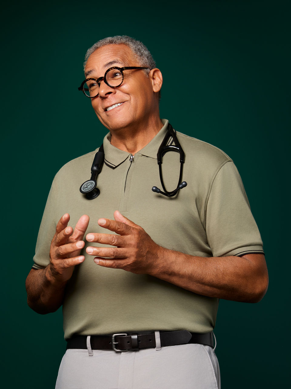 Portrait of a male primary care doctor with Littmann stethoscope around his neck on a dark green background.