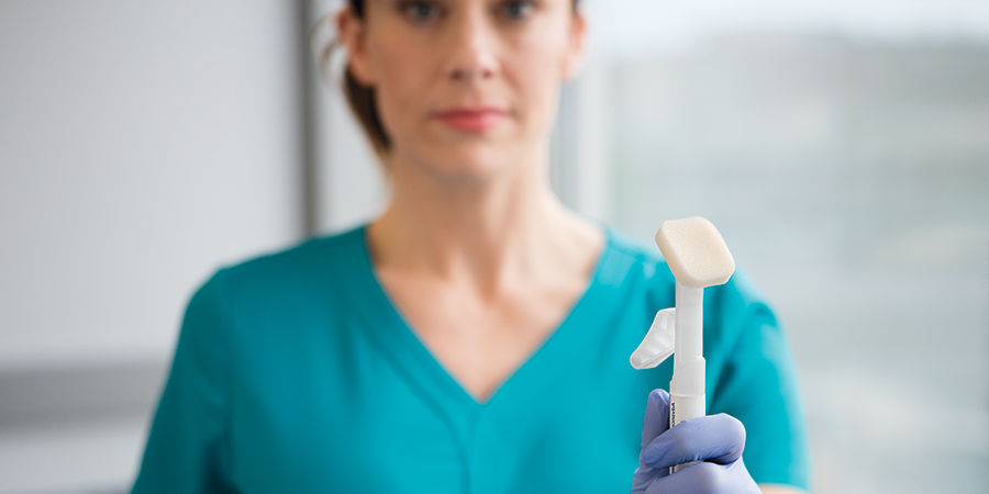 风格化的镜头，聚焦于Cavilon Advanced涂抹器，护理人员戴着手套的手模糊地持有涂抹器。Cavilon英雄形象，裁剪尺寸900x450，RGB色彩模式，JPG格式