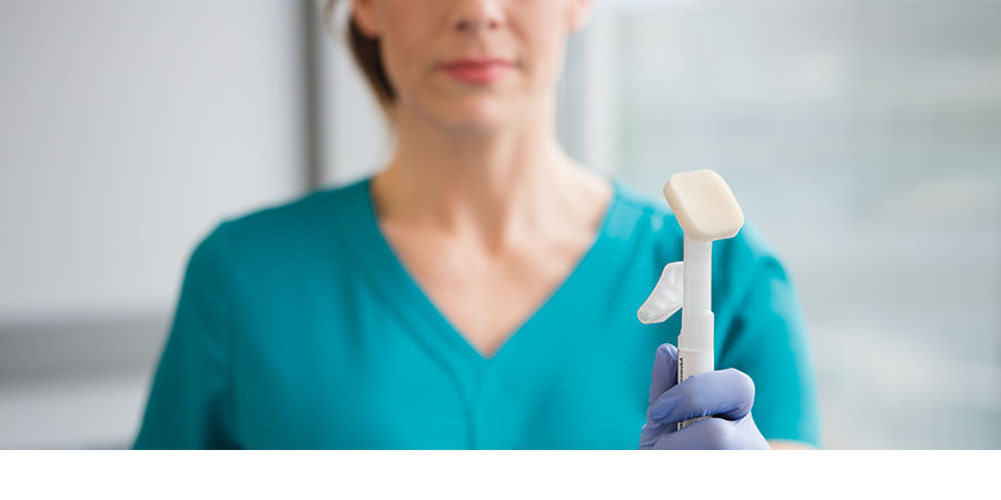 Stylized shot with Cavilon Advanced applicator in focus and nursing holding the applicator with gloved hand out of focus. Cavilon Hero Image, Crop 900x450, rgb, jpg