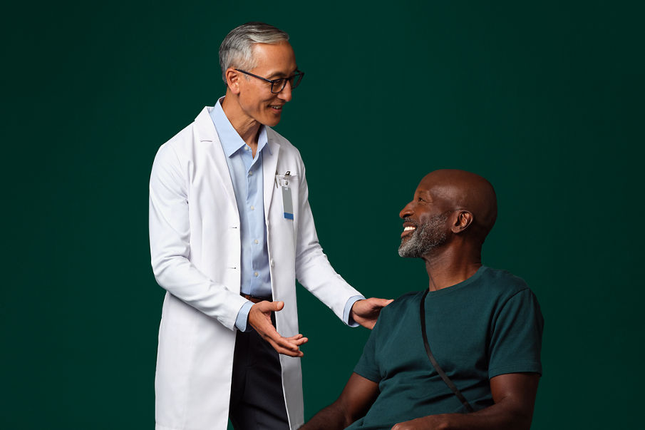 A surgeon in a white coat standing next to and talking with a seated patient who has a Prevena therapy device on their leg.