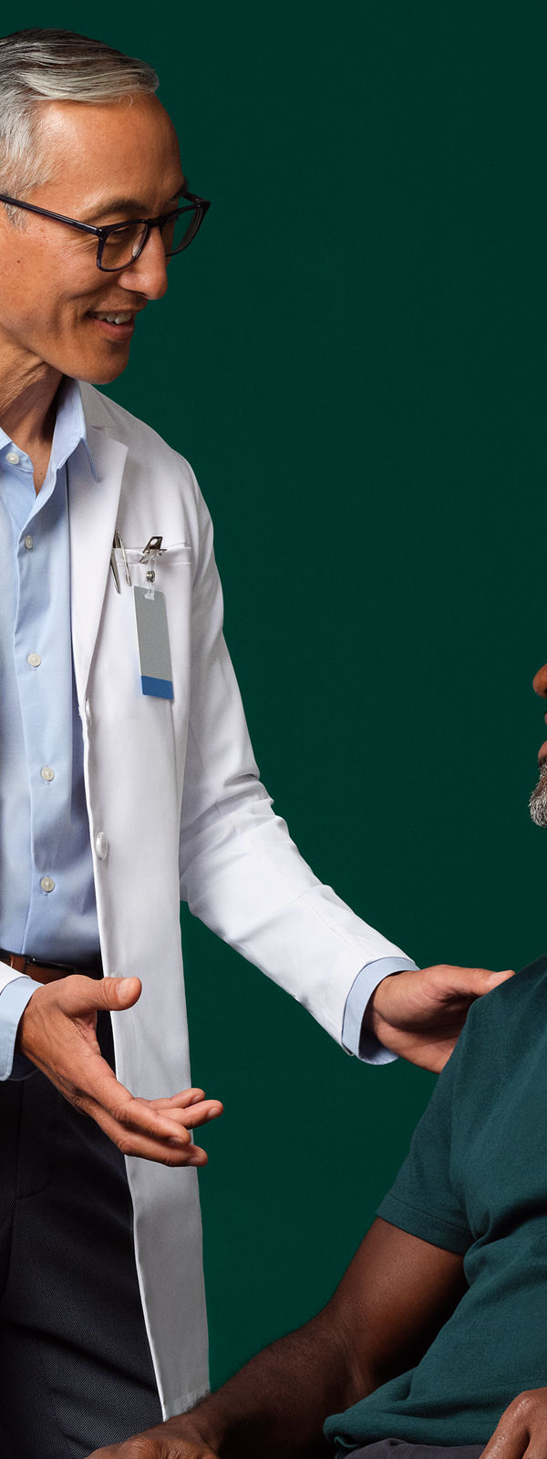 A surgeon in a white coat standing next to and talking with a seated patient who has a Prevena therapy device on their leg.