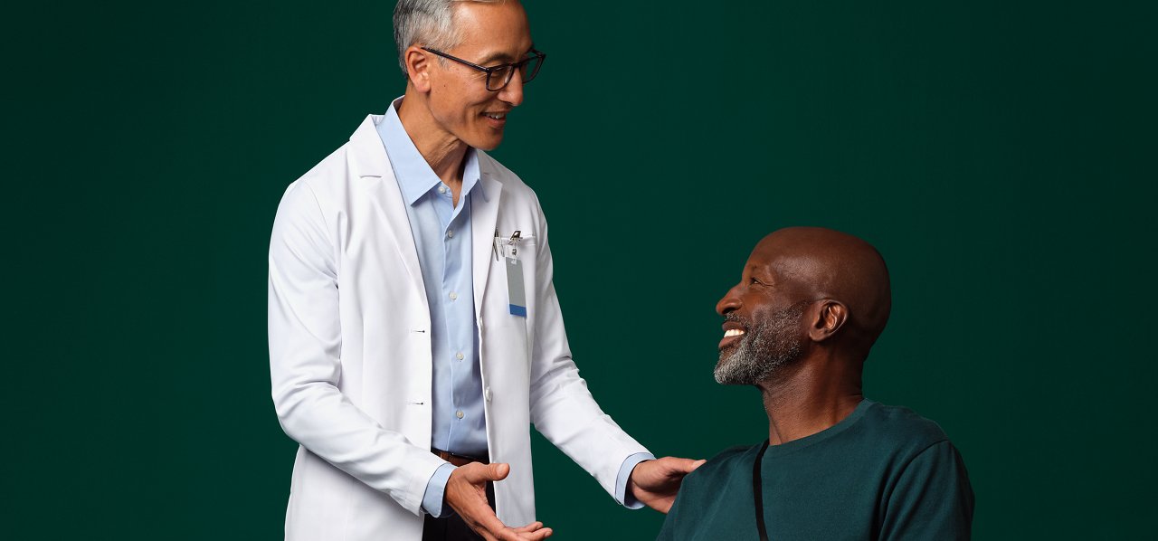 A surgeon in a white coat standing next to and talking with a seated patient who has a Prevena therapy device on their leg.