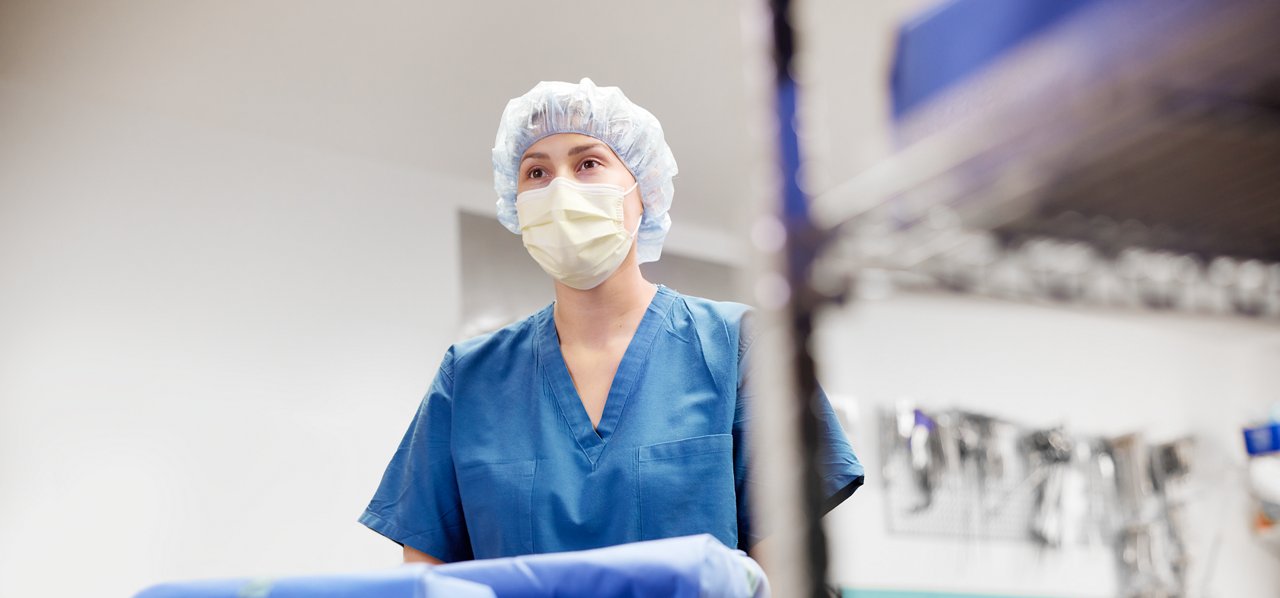 Technician pushing cart filled with packages; sterilization wraps and instruments in background