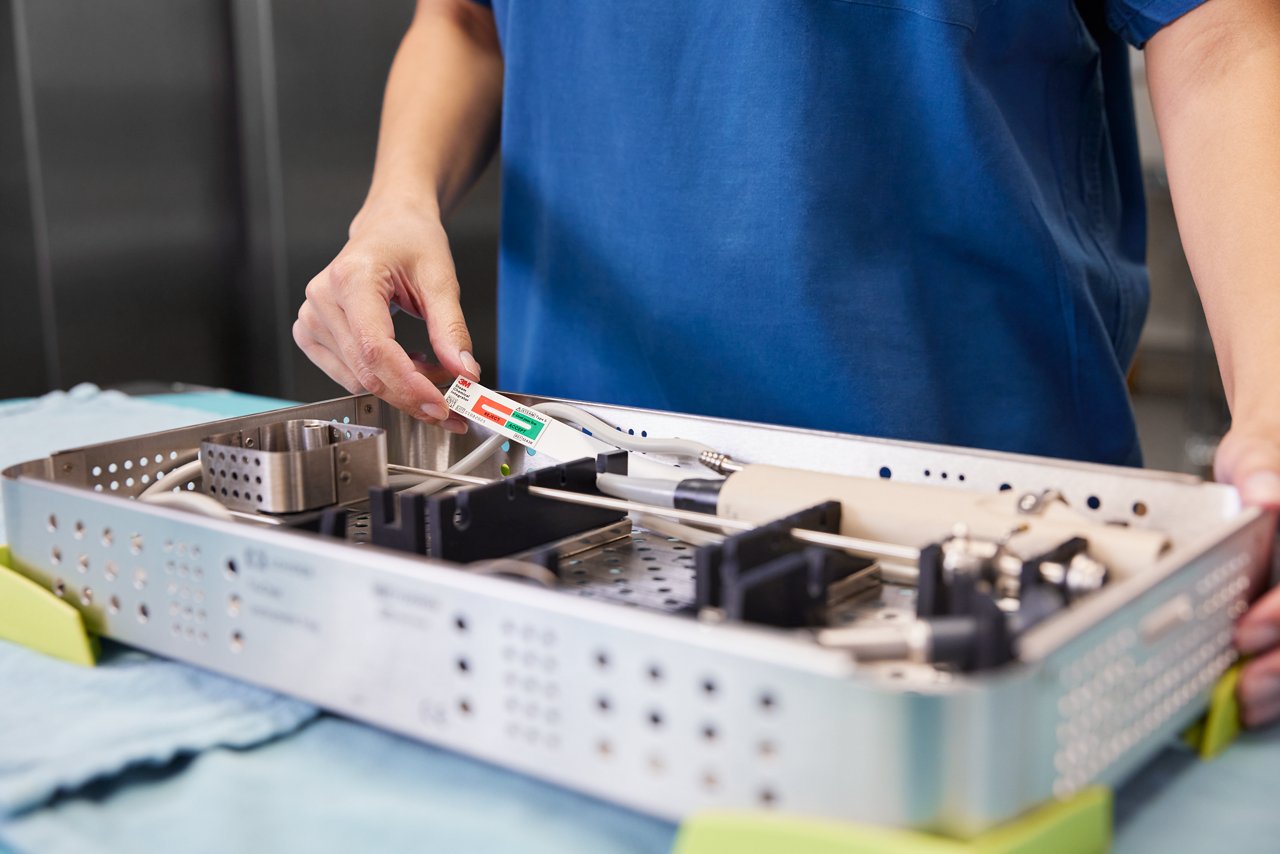 Technician holding 3M™ Attest™ Steam Chemical Integrator, Type 5 (with extender) above tray