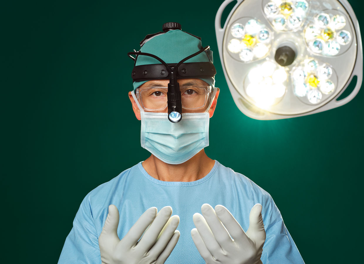 Surgeon in blue scrubs wearing loupes with overhead operating room light.