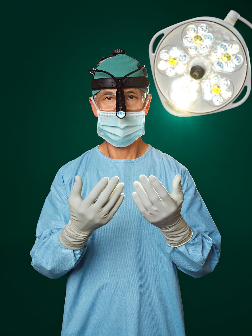 Surgeon in blue scrubs wearing loupes with overhead operating room light.