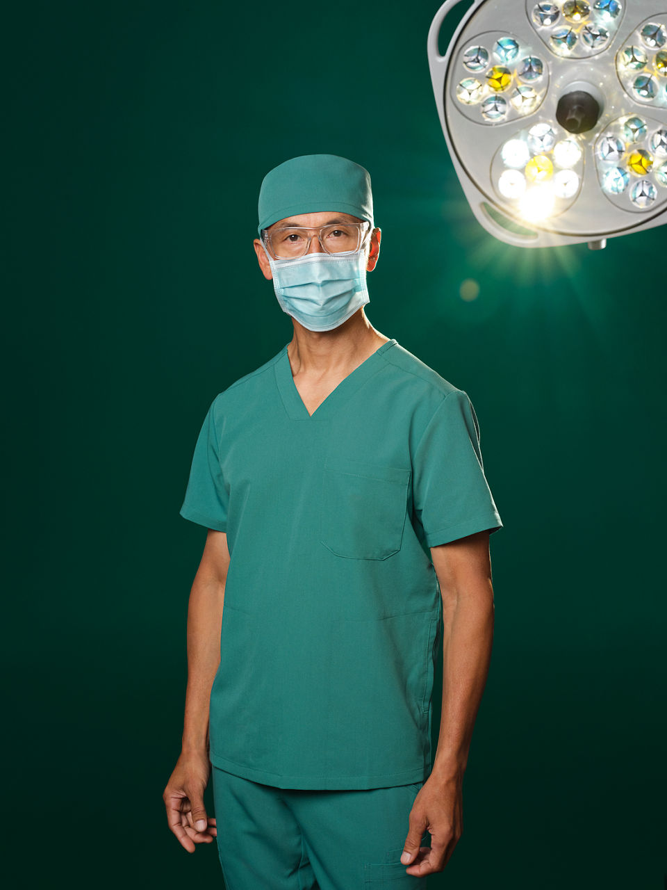 Surgeon in green surgical attire under the operating room ceiling light.