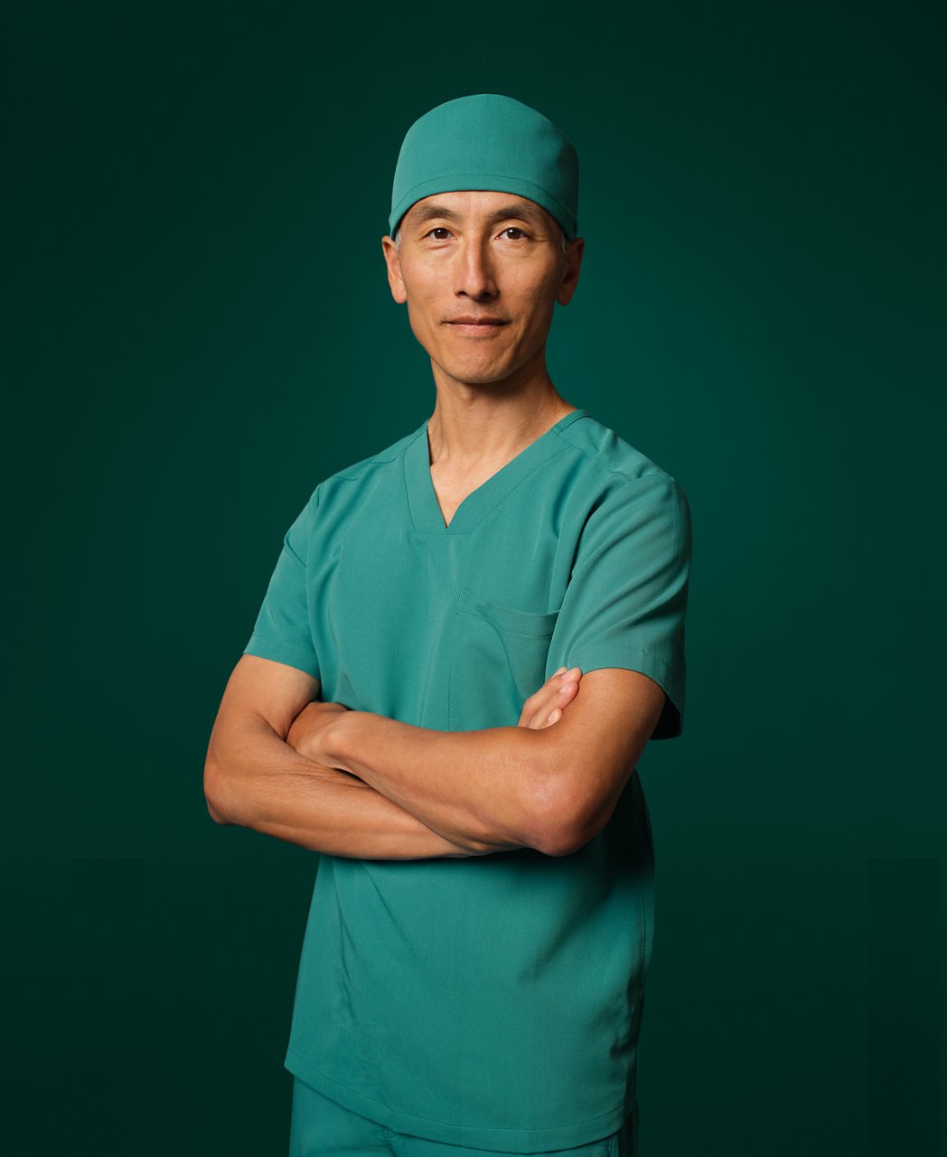 Surgeon in teal surgical uniform with crossed arms.