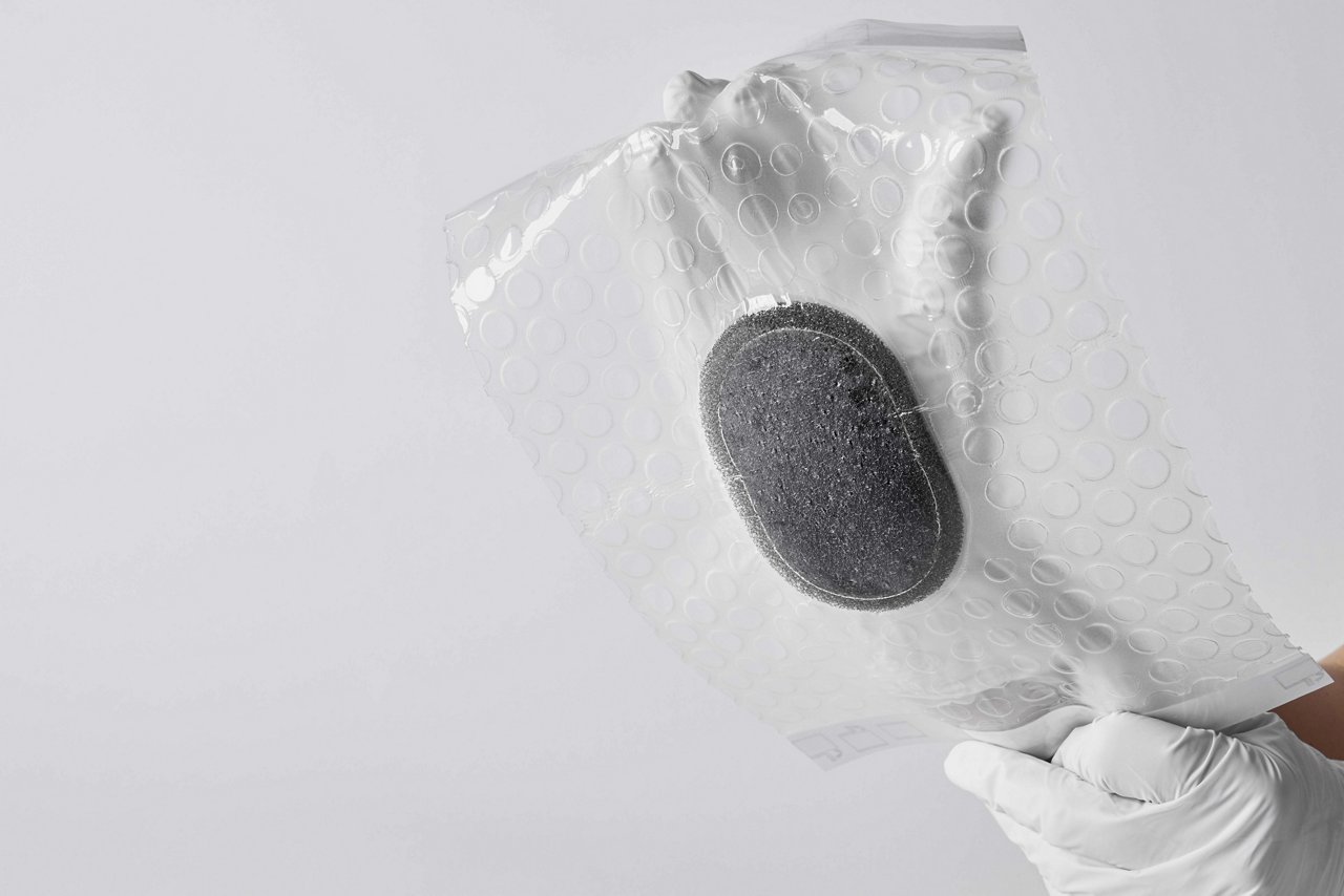 Achteraanzicht van 3M™ V.A.C.® Peel and Place-verband zonder voering, vastgehouden door handen met witte handschoenen op een witte achtergrond.