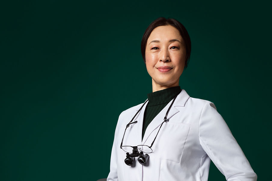 Dentist with loupes around her neck standing next to a stool.