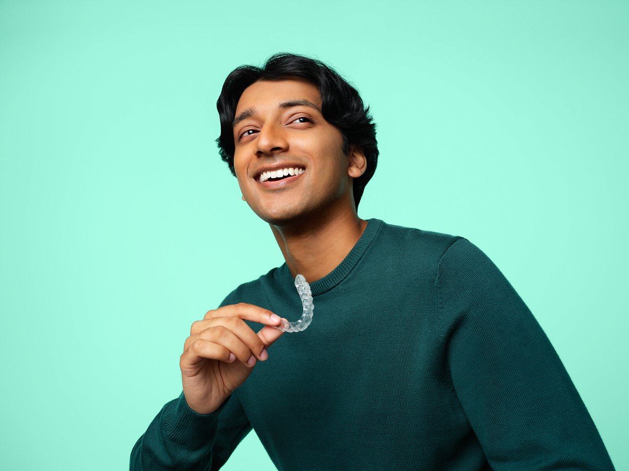  A man holds an aligner like he just took it out of his mouth and smiles with straight, white teeth.