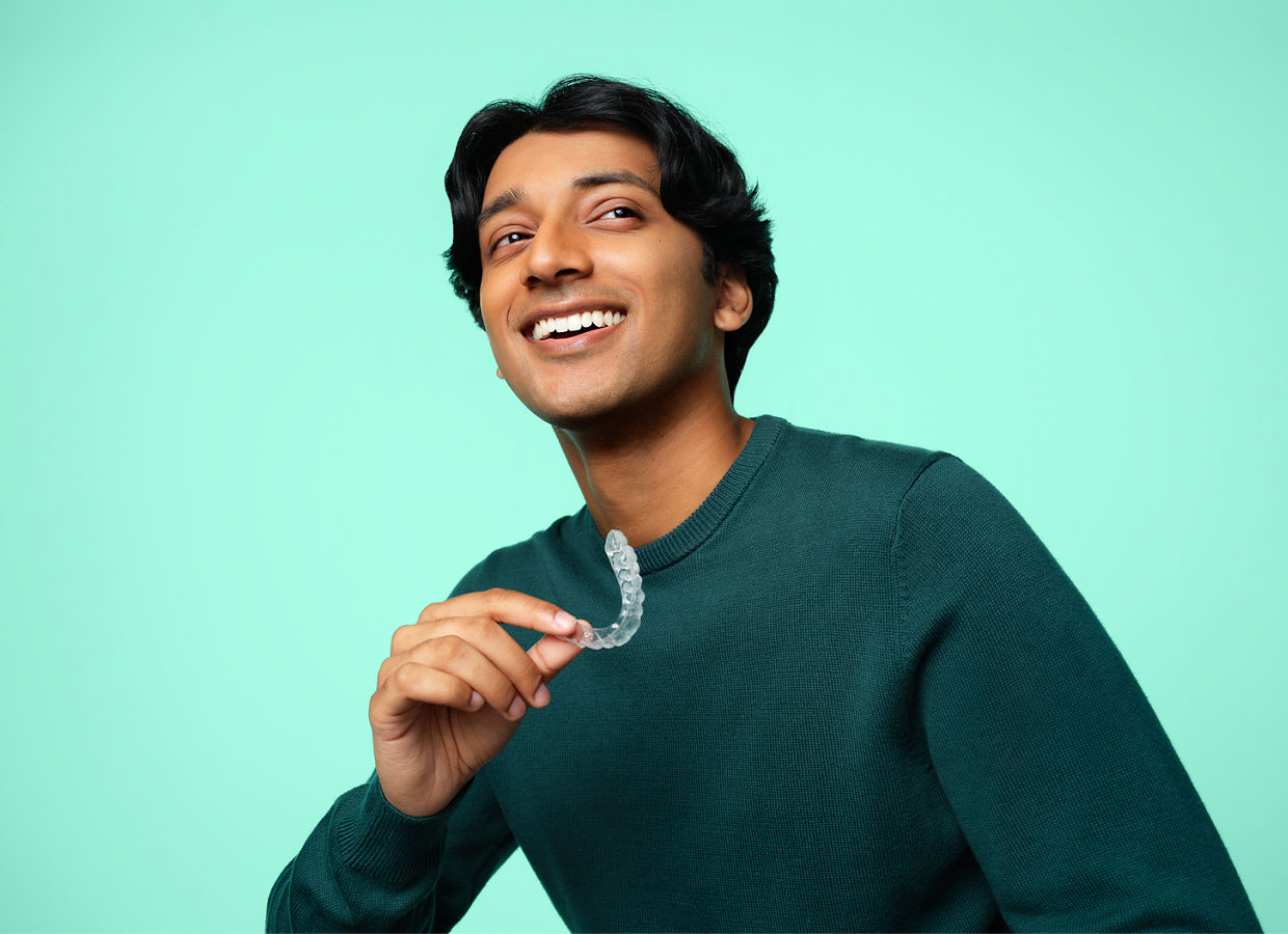 Paciente ortodôntico do sexo masculino com camisa verde sorridente segurando o alinhador Clarity