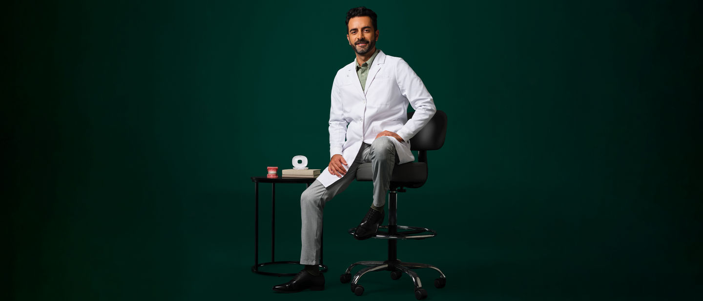 Orthodontist in a white coat sitting on a stool next to a small table displaying an aligner case and typodent.